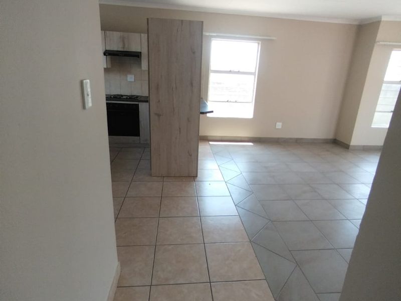 An open-plan living and kitchen area featuring neutral tiled flooring, modern cabinetry, and integrated kitchen appliances in a clean, vacant space.