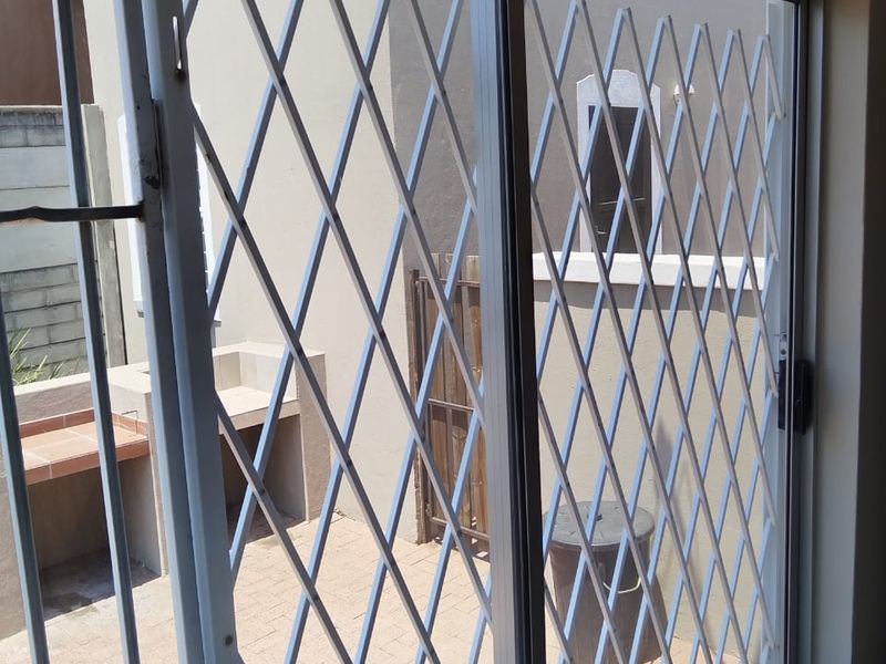 A covered patio area featuring a built-in braai, paved flooring, and a sliding glass door with a security gate.