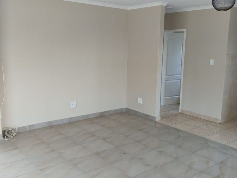 A bright, empty living area featuring neutral wall paint, ceramic floor tiles, and modern ceiling lighting fixtures.
