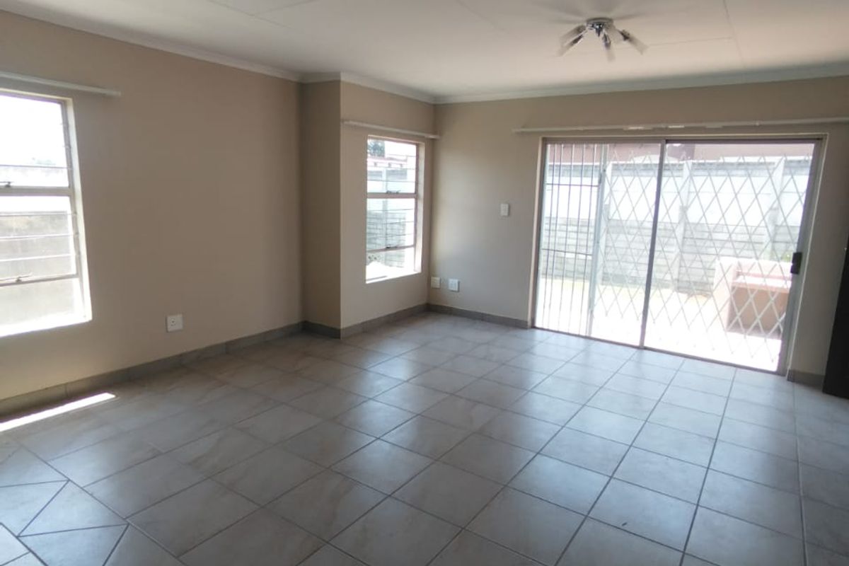 A spacious, empty living room featuring neutral tiled flooring, large windows, and a sliding glass door leading to an outdoor area.