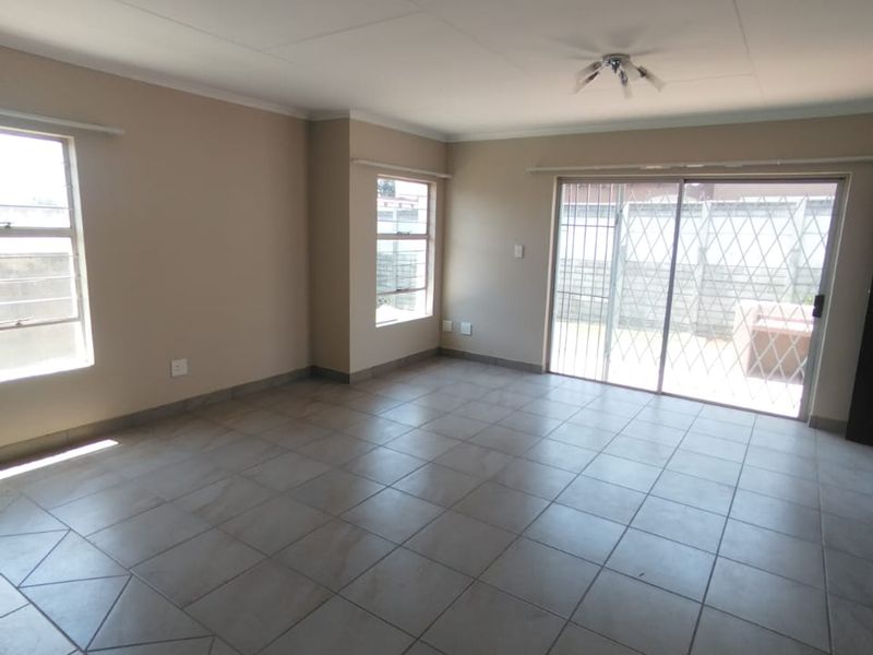 A spacious, empty living room featuring neutral tiled flooring, large windows, and a sliding glass door leading to an outdoor area.