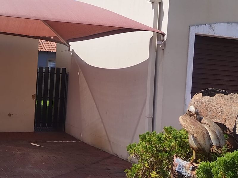 A paved outdoor area featuring a shade sail, a side gate, and a low-maintenance garden bed with decorative rock and shrubbery.
