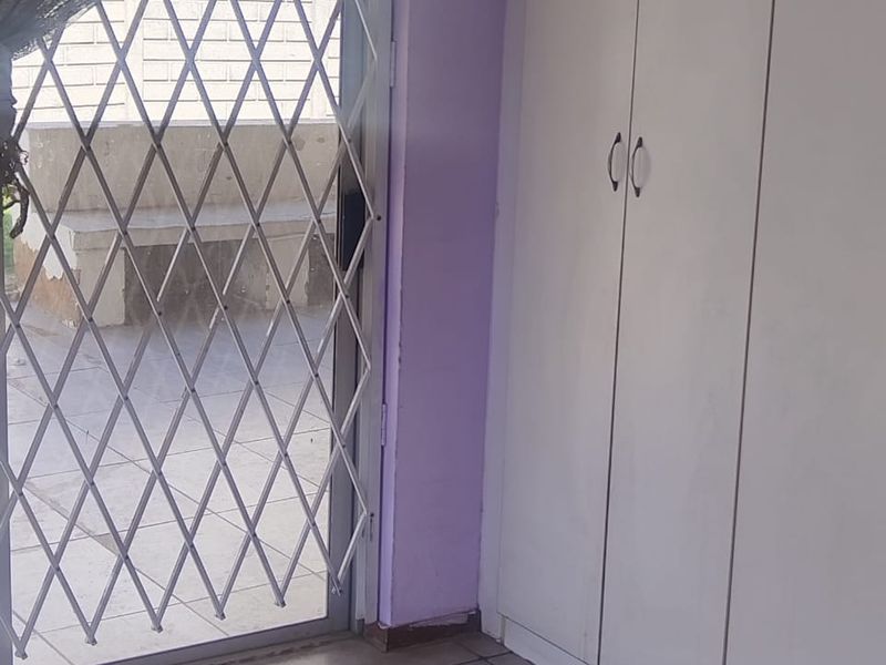 A bedroom interior featuring built-in cupboards, tiled flooring, and a sliding glass door with a security gate leading to an outdoor area.