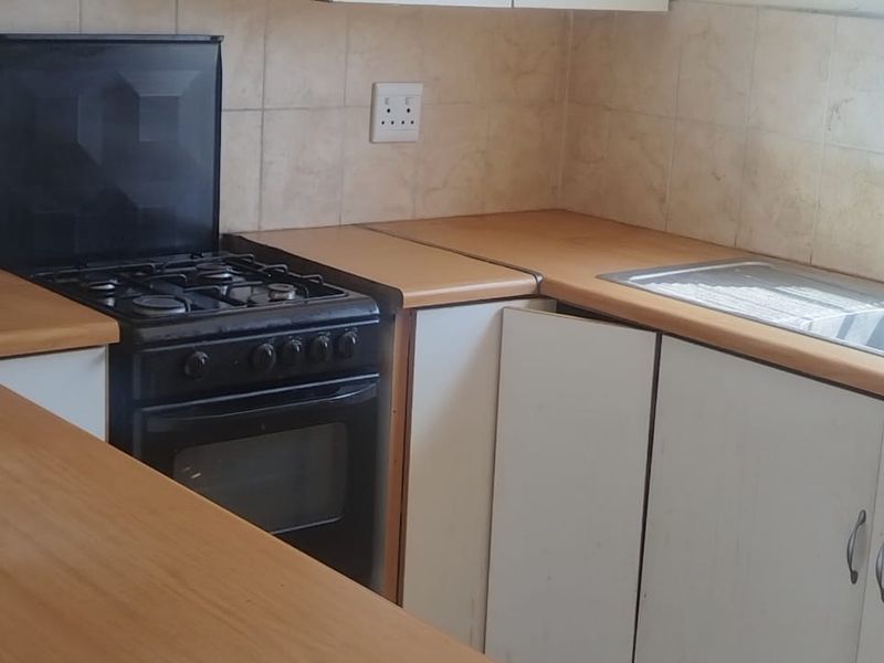 A functional kitchen featuring white cabinetry, wood-look laminate countertops, a built-in gas stove with extractor fan, and tiled splashbacks.
