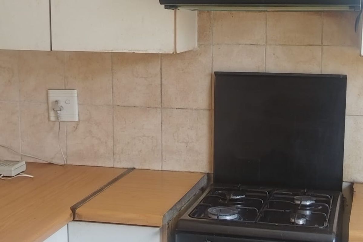 A compact kitchen area featuring white cabinetry, laminate countertops, a built-in gas stove, and a black extractor fan.