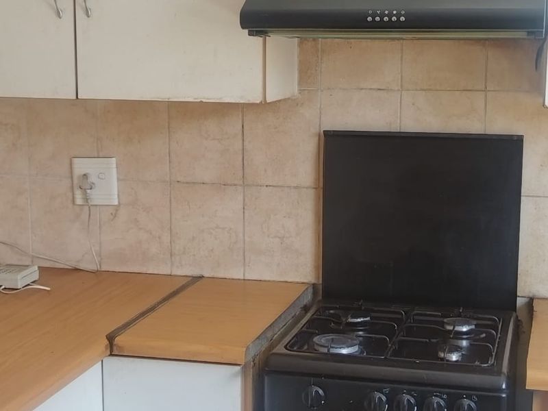 A compact kitchen area featuring white cabinetry, laminate countertops, a built-in gas stove, and a black extractor fan.