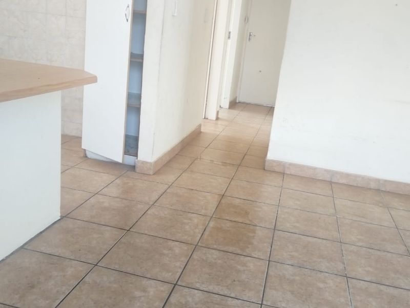 An empty interior space featuring tiled flooring, a built-in storage cupboard, and access to a hallway leading to other rooms.