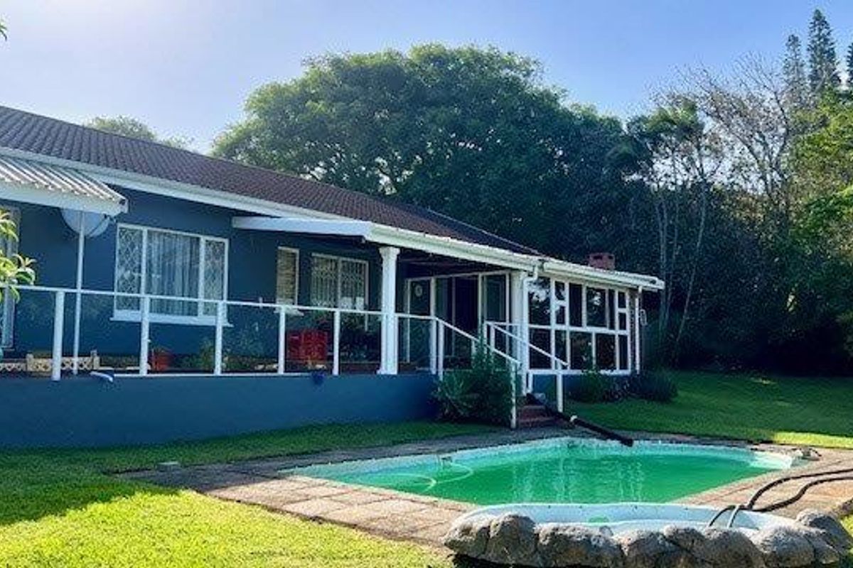 Rear view of the house featuring a swimming pool, raised patio area with white railings, and a spacious garden setting.
