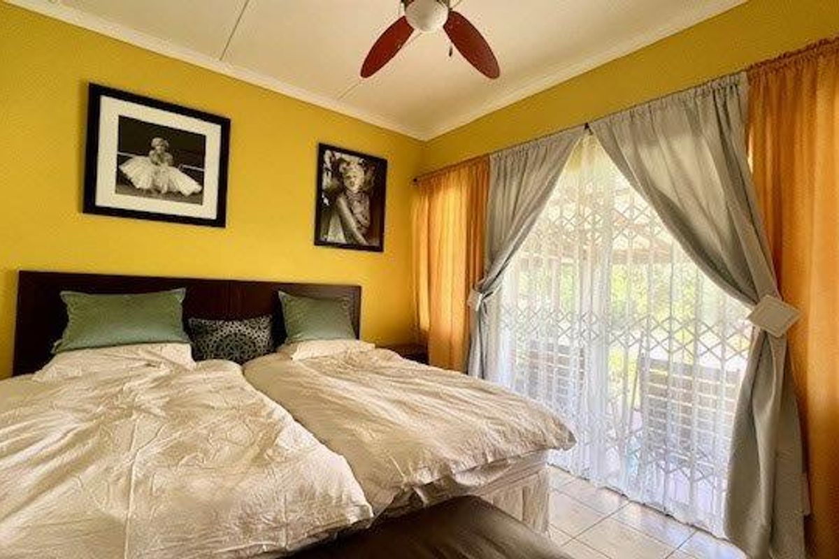 A bedroom featuring a ceiling fan and sliding glass doors with security gates, providing access to an outdoor area.