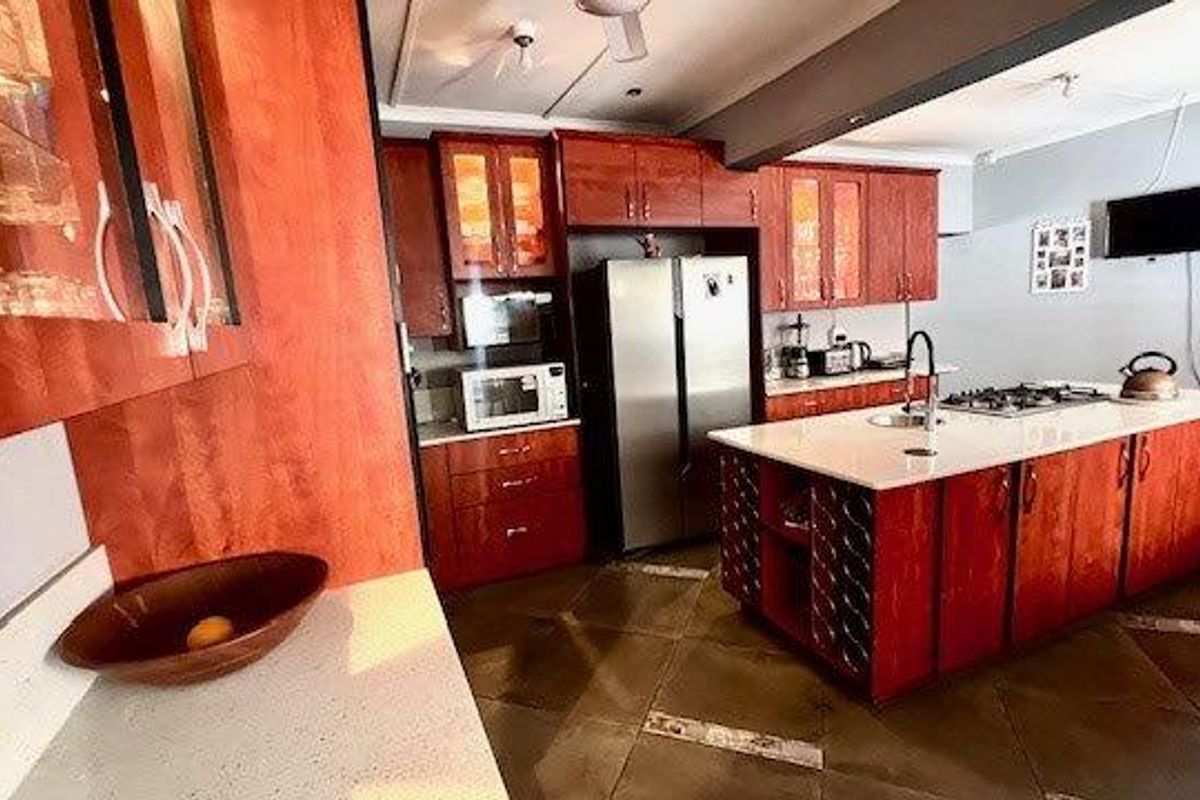 Spacious kitchen featuring warm-toned wooden cabinetry, a central island with a built-in hob and sink, and stone countertops.