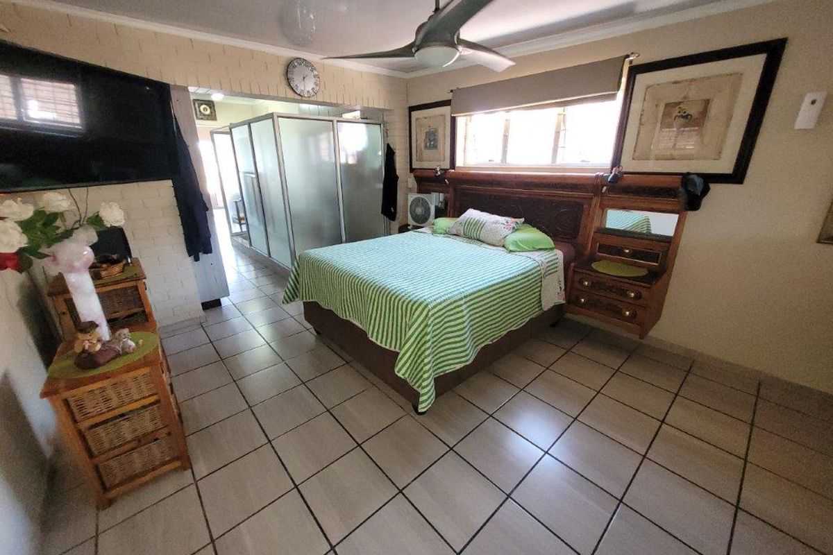 Spacious bedroom featuring tiled flooring, a ceiling fan, and a built-in headboard, with an adjoining en-suite bathroom area visible through a sliding door.