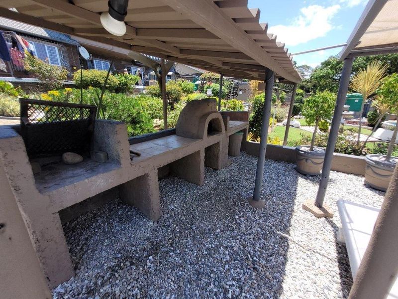 Outdoor entertainment area featuring a built-in braai and pizza oven under a pergola, set on a gravel patio.