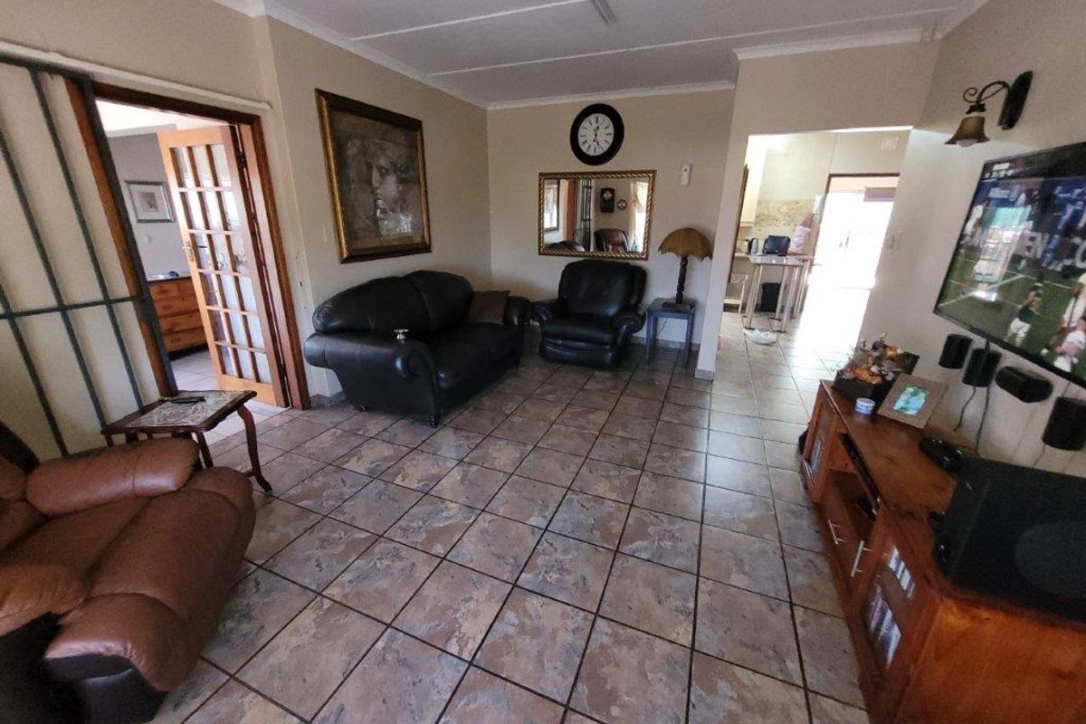 A living room featuring tiled flooring and french doors leading to an adjacent room, with an open transition to the kitchen area.