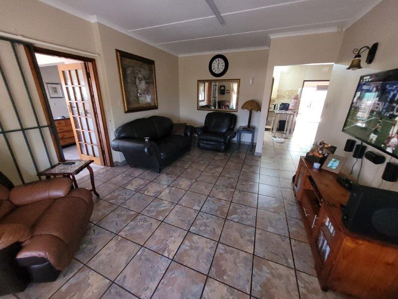 A living room featuring tiled flooring and french doors leading to an adjacent room, with an open transition to the kitchen area.