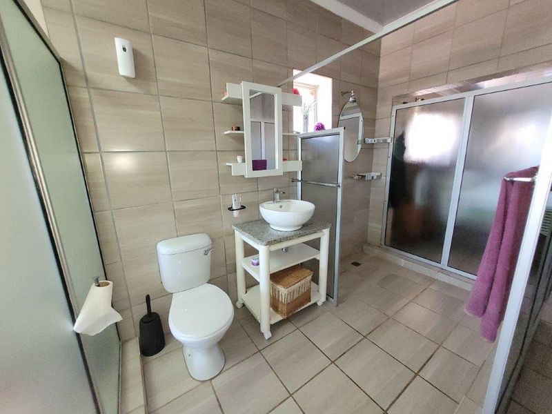 A well-maintained bathroom featuring neutral ceramic tiling, a modern vessel sink vanity, and a glass-enclosed shower area.