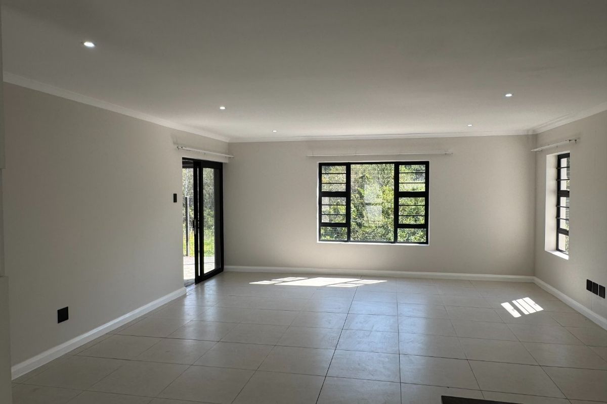 A bright, spacious, and empty living area featuring neutral tiled flooring, recessed downlights, and large aluminium-framed windows providing natural light.