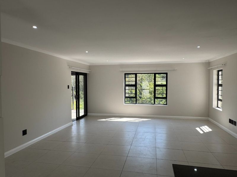A bright, spacious, and empty living area featuring neutral tiled flooring, recessed downlights, and large aluminium-framed windows providing natural light.