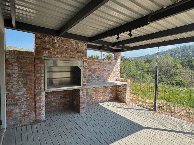 Covered outdoor patio featuring a built-in brick braai, concrete prep surface, and paved flooring, overlooking a scenic landscape.