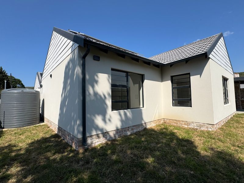 Rear view of a modern house featuring a tiled roof, solar panels, aluminium window frames, and an external water storage tank.