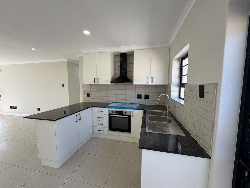 Modern kitchen featuring granite countertops, built-in oven, extractor fan, and stainless steel double sink with a clean tiled backsplash.
