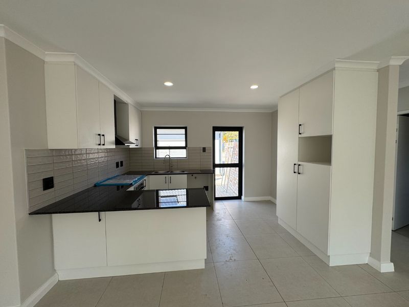 Modern kitchen featuring white cabinetry, dark granite countertops, subway tile backsplash, and tiled flooring with direct access to the exterior.