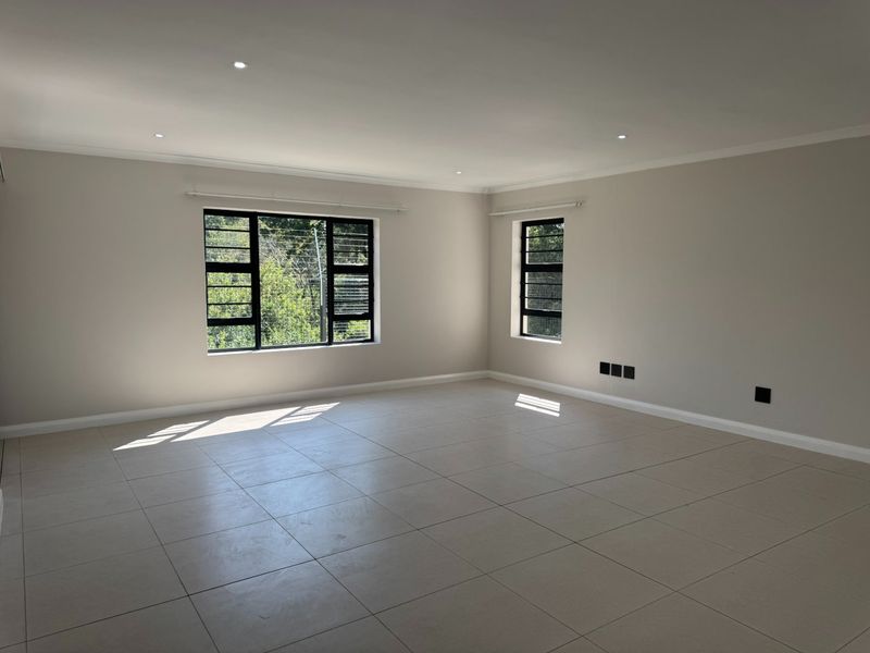 A bright, spacious, and empty living area featuring neutral tiled flooring, modern recessed downlights, and large black aluminium-framed windows.