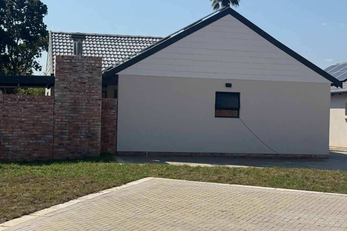 Rear view of the property featuring a brick chimney, tiled roof, solar panels, and a paved driveway area.