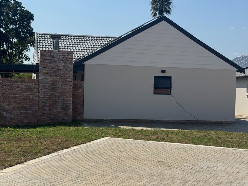 Rear view of the property featuring a brick chimney, tiled roof, solar panels, and a paved driveway area.