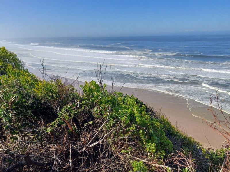 A scenic elevated view overlooking the coastline, sandy beach, and ocean waves from the vacant residential property.