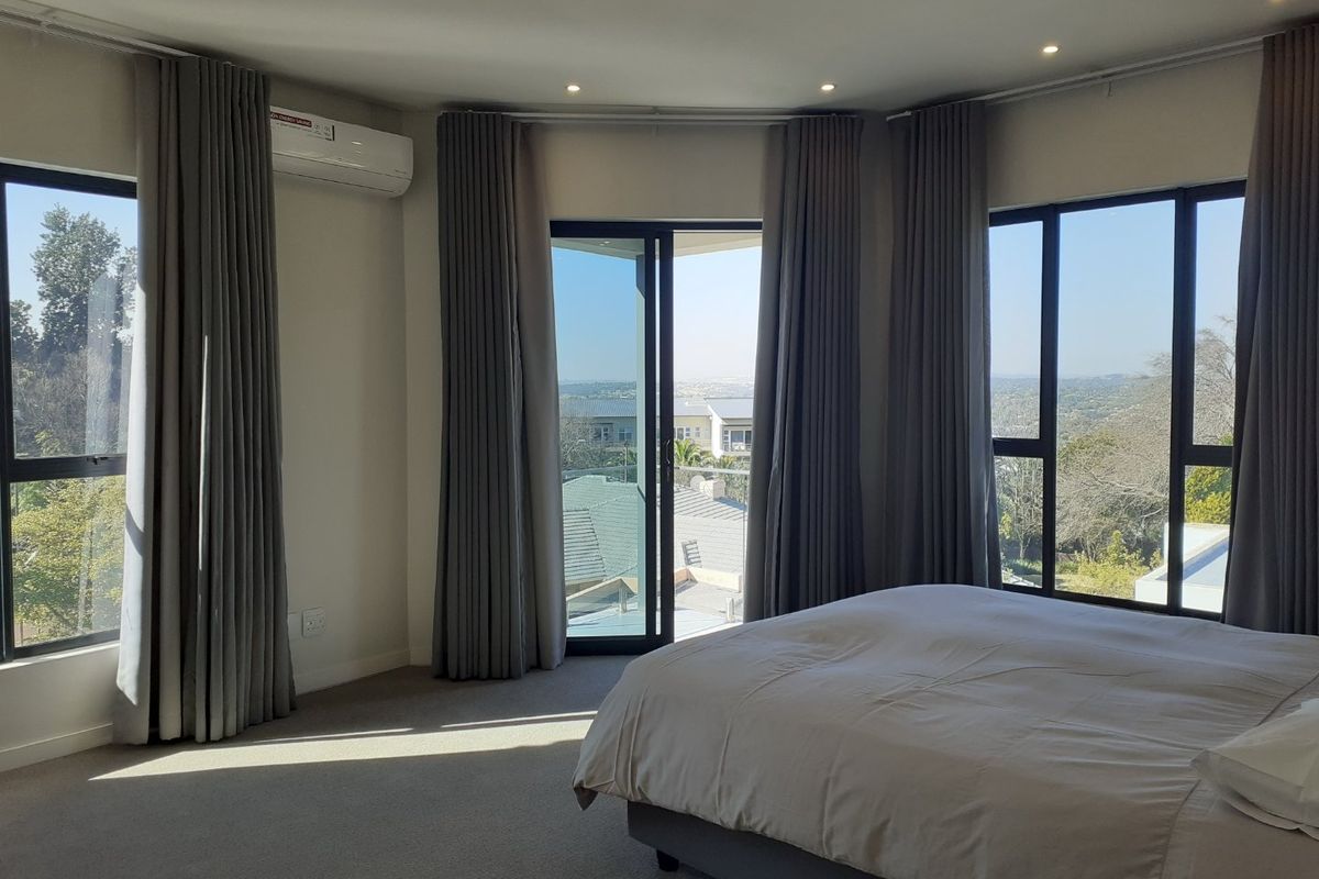 Spacious bedroom featuring large windows, sliding door access to a balcony, neutral carpeting, and a wall-mounted air conditioning unit.