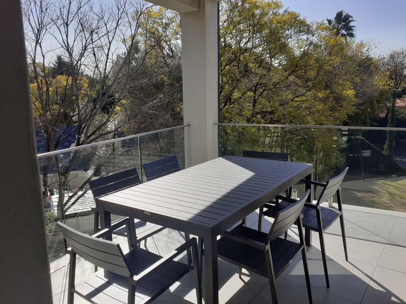 A modern balcony featuring a glass balustrade, tiled flooring, and a structural pillar, offering an elevated view of the surrounding trees.