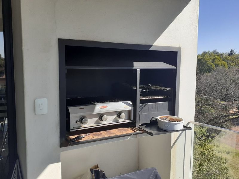 A balcony area featuring a built-in braai unit with a glass balustrade, offering an outdoor space suitable for entertaining.