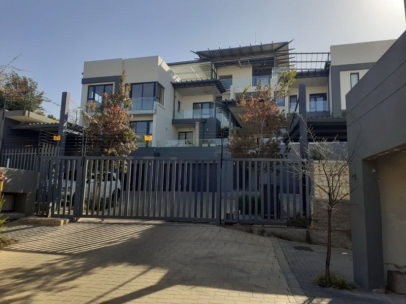 A modern multi-level apartment complex featuring a secure gated entrance, paved driveway, and contemporary architectural design with glass balustrades.