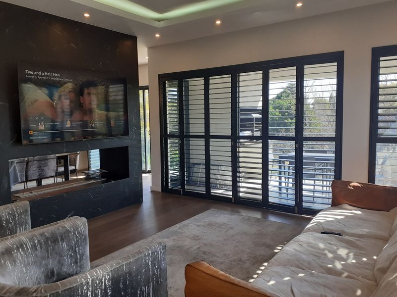Modern living room featuring a striking black marble-look feature wall with a built-in fireplace, timber flooring, and black aluminium folding shutters leading to the balcony.