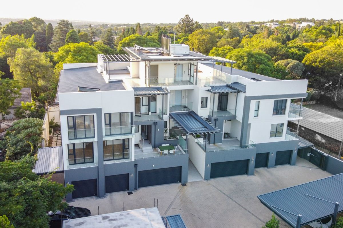 Aerial view of a modern multi-level apartment complex featuring contemporary architecture, glass balconies, paved driveway, and integrated garage access.