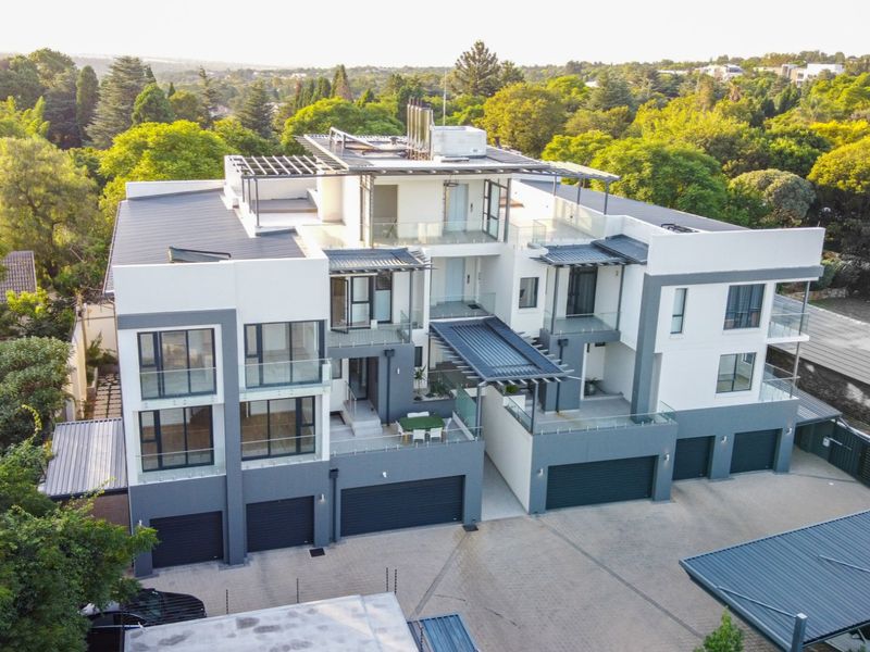 Aerial view of a modern multi-level apartment complex featuring contemporary architecture, glass balconies, paved driveway, and integrated garage access.