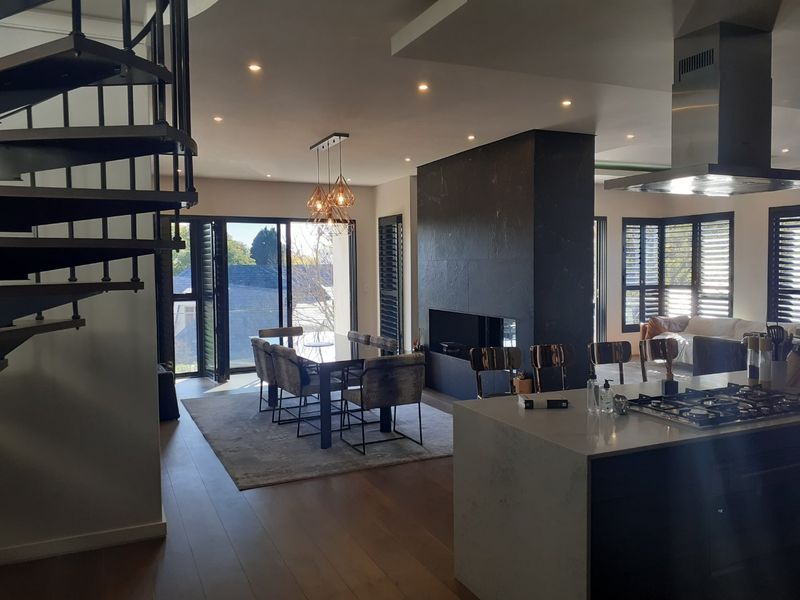 Spacious open-plan living area featuring a modern kitchen island, striking stone fireplace, spiral staircase, and timber flooring with abundant natural light.