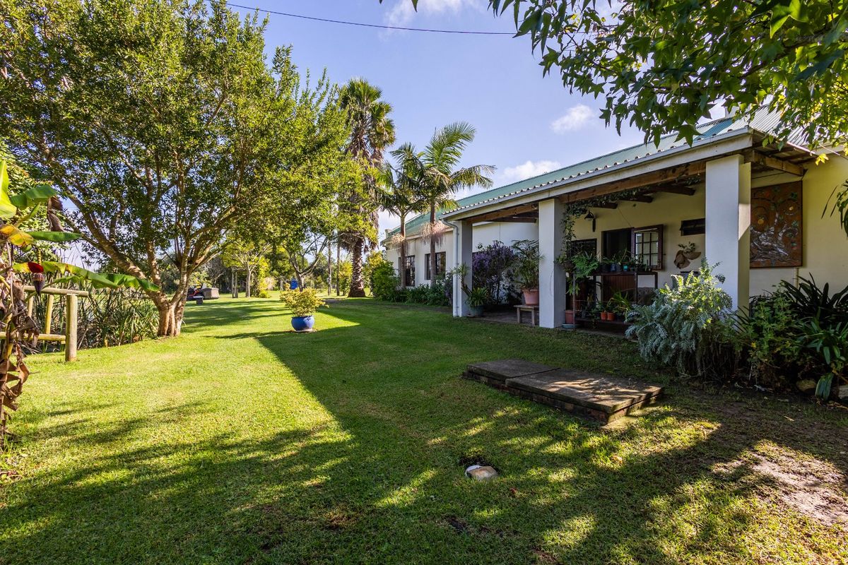 A spacious rear garden featuring a covered patio area with concrete pillars, overlooking a well-maintained lawn and mature trees on the farm property.