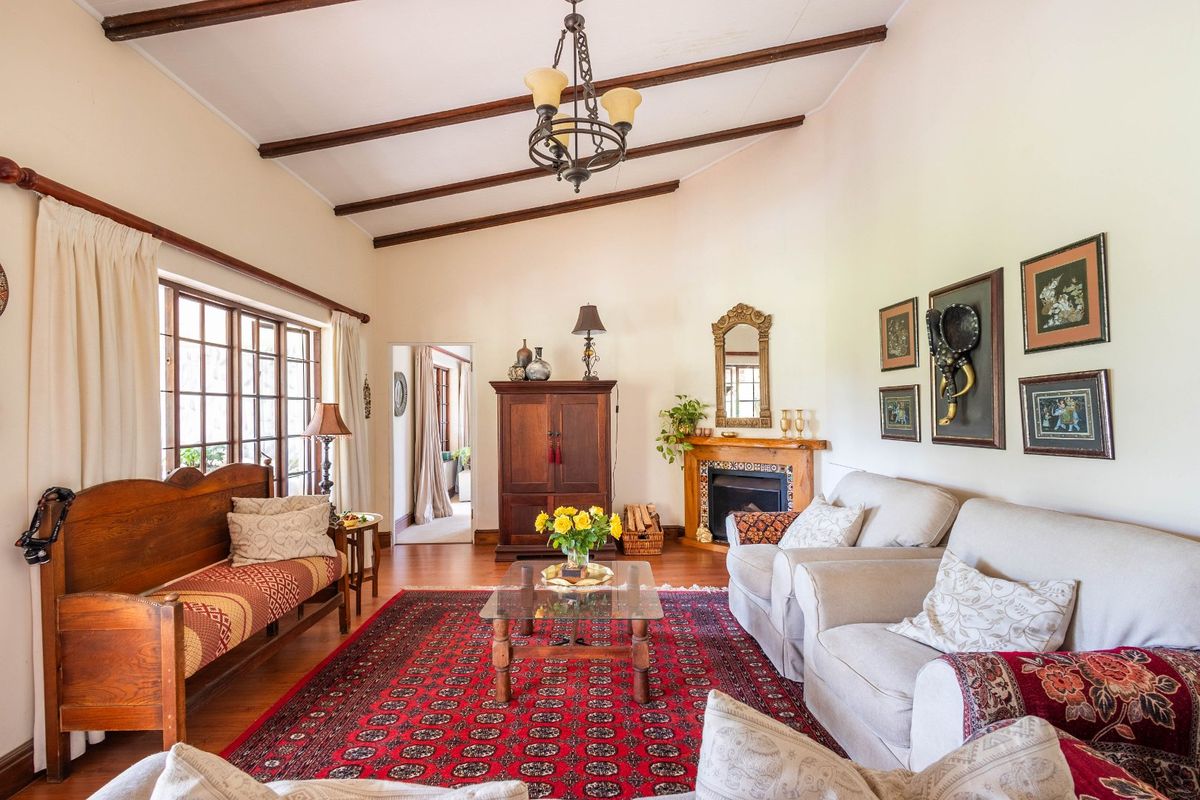 Spacious living room featuring high ceilings with exposed timber beams, hardwood flooring, and a traditional fireplace with a timber mantel.