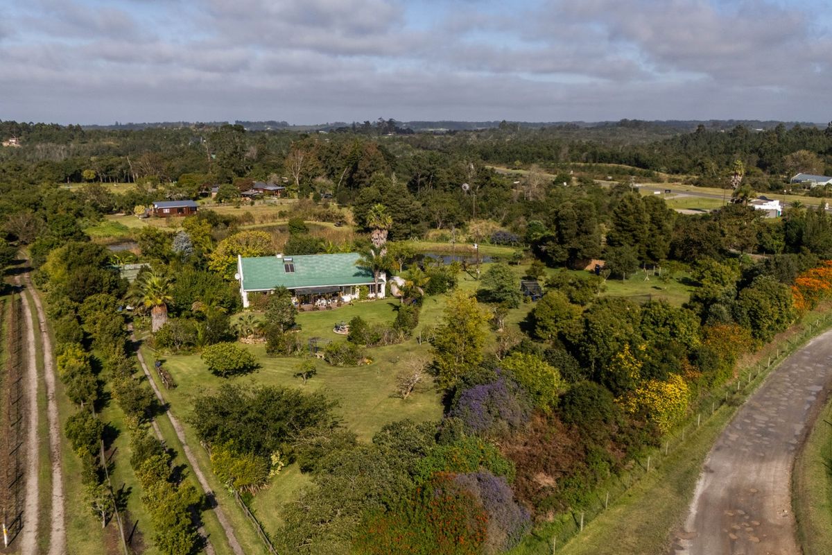 Aerial view of a rural farm property featuring a main residence with a green metal roof, expansive garden, and surrounding landscape.
