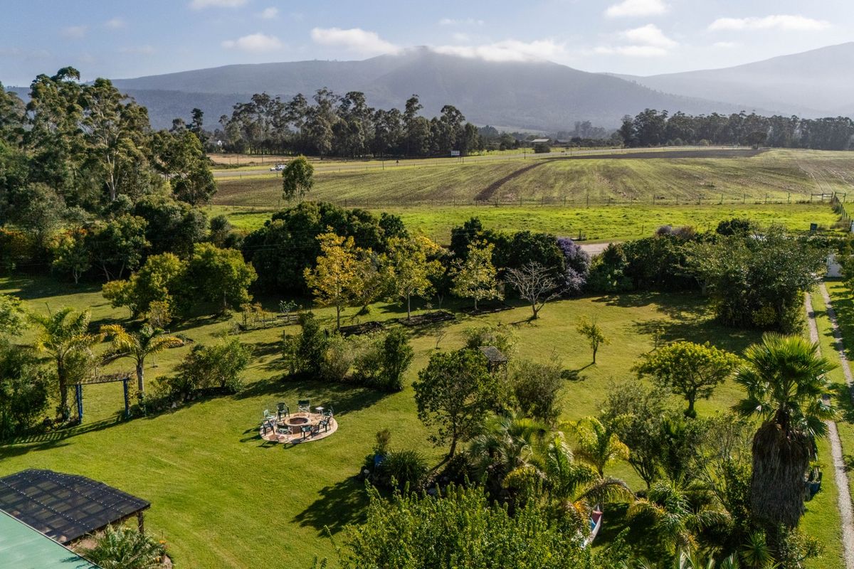Aerial view of a spacious, well-maintained farm garden featuring mature trees, a central fire pit area, and expansive rural landscape views.