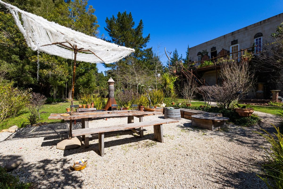 A rustic rear garden area featuring a gravel patio, outdoor fireplace, and elevated timber decking attached to the main farm building.