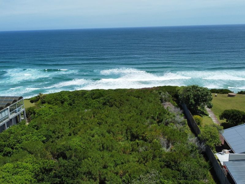 An aerial view of a vacant residential plot featuring coastal vegetation, direct ocean views, and established boundary fencing.