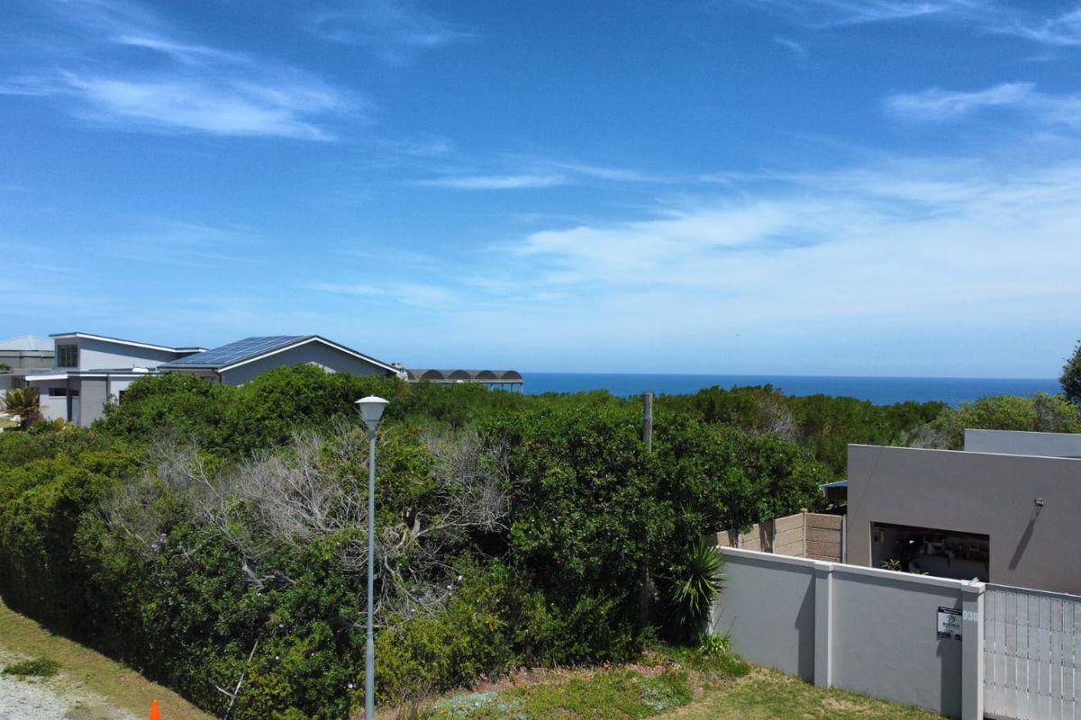 An elevated view of the residential plot featuring dense coastal vegetation, boundary walls, and a clear horizon line overlooking the ocean.