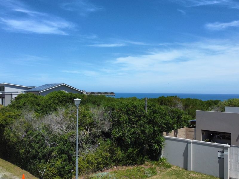 An elevated view of the residential plot featuring dense coastal vegetation, boundary walls, and a clear horizon line overlooking the ocean.