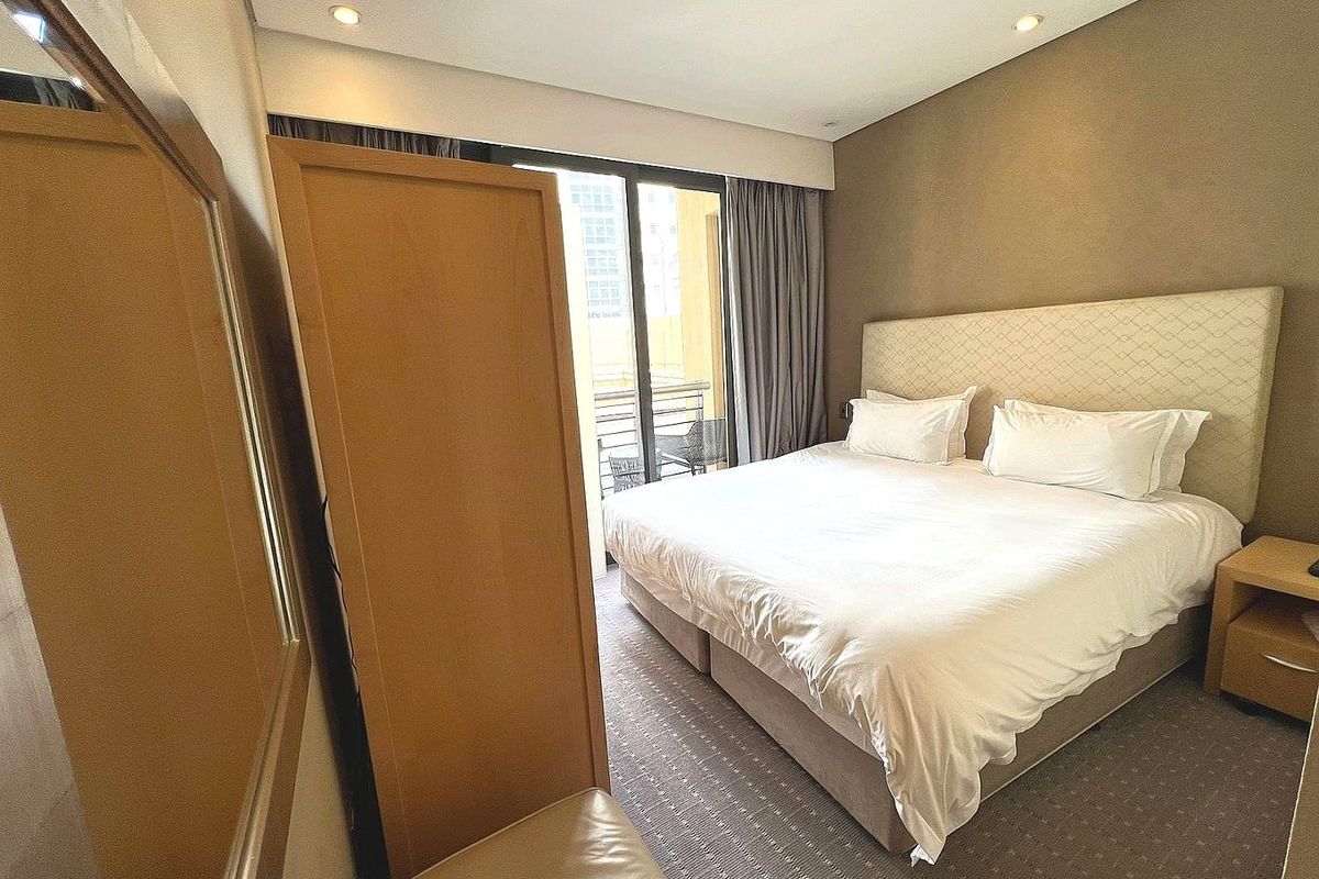 A well-maintained bedroom featuring a large upholstered headboard, recessed lighting, and direct access to a private balcony through sliding glass doors.