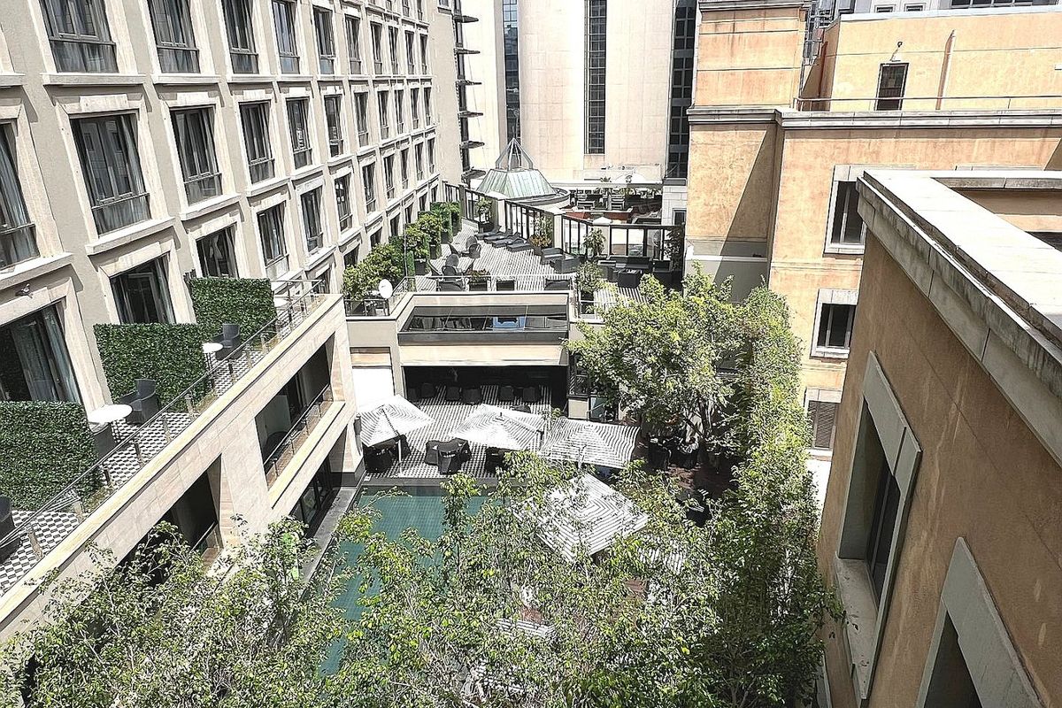 An elevated aerial view of a central courtyard featuring a swimming pool, landscaped trees, and surrounding multi-story apartment building balconies.