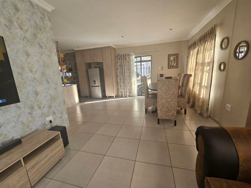 Spacious open-plan living and dining area featuring neutral tiled flooring, recessed lighting, and a seamless transition to the kitchen and outdoor access.