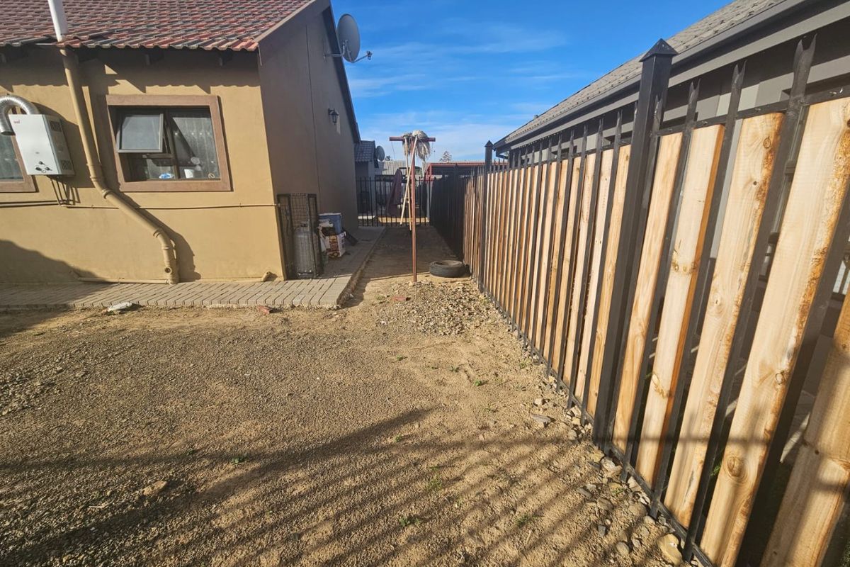 A side yard area featuring a paved walkway, gas geyser, and a modern timber and metal boundary fence.
