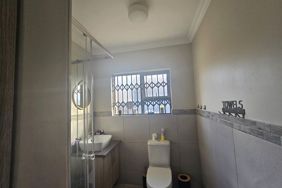 A functional bathroom featuring a vanity with a vessel sink, a toilet, and a glass-enclosed shower with neutral wall tiling.
